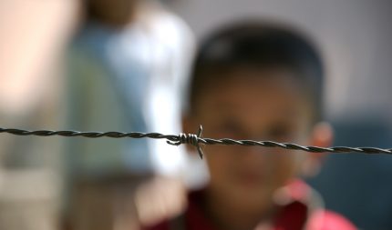 Imagem mostra criança desfocada atrás de uma cerca de arame farpado