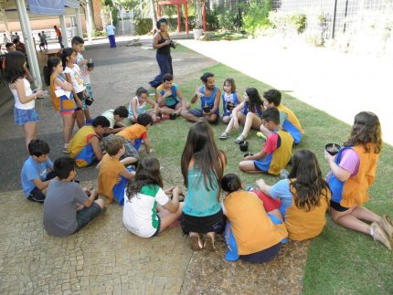 Crianças faze, rodo de conversa com a presença de índios vestindo suas roupas típicas