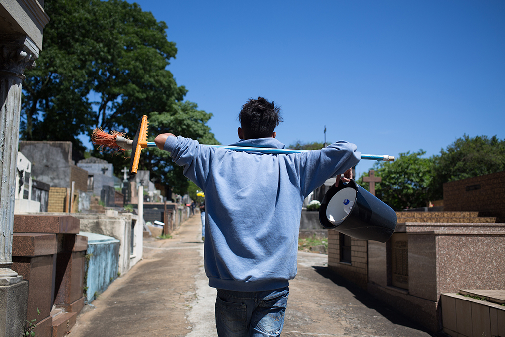 Garoto de costas carrega utensílios de limpeza no Cemitério do Araçá, em São Paulo