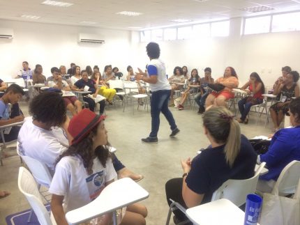 Grupo sentado em carteiras em circulo e uma pessoa no centro durante discussão no simpósio