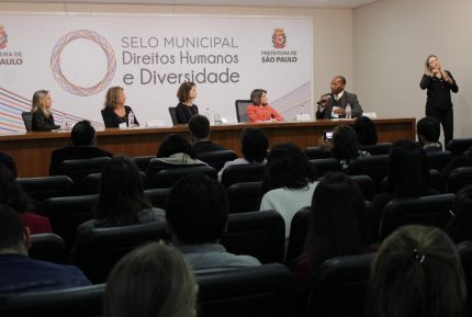 Foto da plateia e da mesa onde era lançado o selo municipal dos direitos humanos
