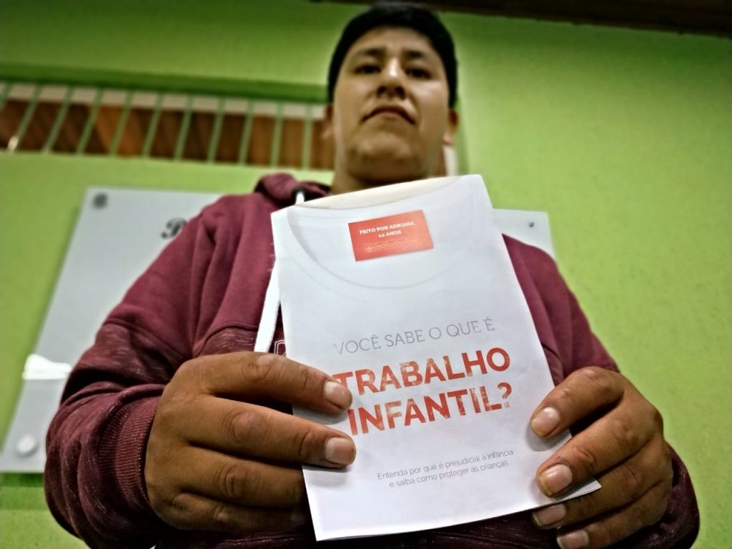Homem boliviano segura folder da campanha trabalho infantil na indústria da moda.